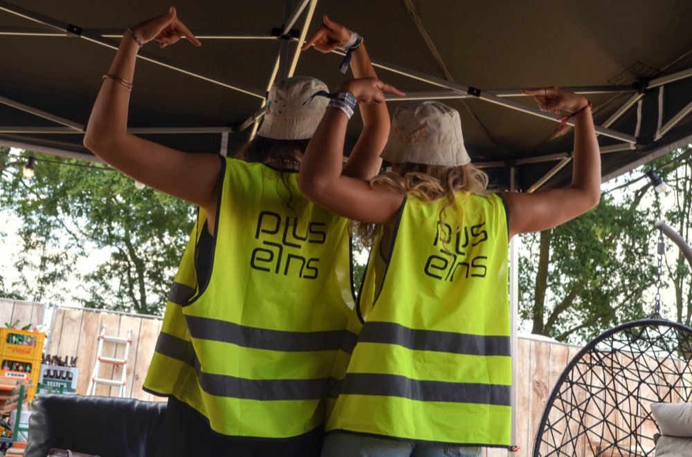 Zwei Teammitglieder zeigen auf das pluseins Logo ihrer Warnwesten